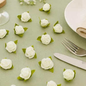 Könnte beinhalten: Eine Tischdekoration mit weißen Rosen, einem Teller, Besteck und einer Serviette. Die kleinen weißen Rosen haben grüne Blätter. Ein Holzherz mit den Buchstaben "E&K" liegt auf der Serviette.