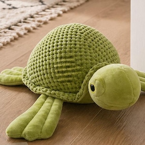 Può includere: Un fermaporta a forma di tartaruga verde. La tartaruga ha un guscio strutturato, arti a forma di pinna e una testa rotonda con un occhio nero. Realizzato in materiale morbido per impedire la chiusura delle porte.