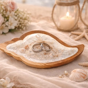 May include: A wooden ring holder shaped like a leaf, filled with sand and two silver rings. The holder is surrounded by seashells, starfish, and candles, creating a beach-themed wedding display.