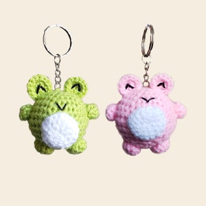 May include: Two crocheted frog keychains, one green and one pink, with white bellies and black eyes.