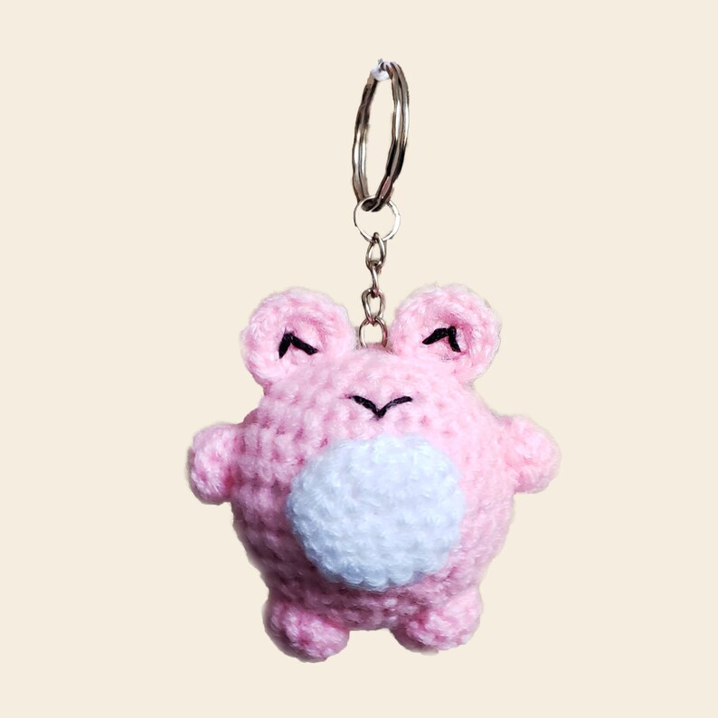 May include: Pink crocheted frog keychain with a white belly and black eyes.