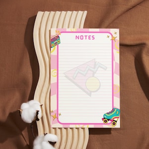 Puede incluir: Un bloc de notas rectangular con un borde rosa y la palabra NOTES impresa en la parte superior. El papel presenta un fondo ondulado en rosa claro y blanco con ilustraciones de un radiocasete, un patín, estrellas y un diseño triangular.
