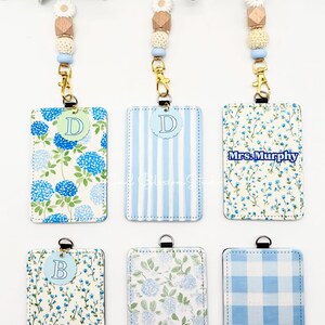 May include: Six rectangular ID badge holders with lanyards featuring beaded accents. The holders display various blue and white patterns including hydrangeas, stripes, floral prints, and gingham. Some holders feature circular letter tags or the text Mrs. Murphy.