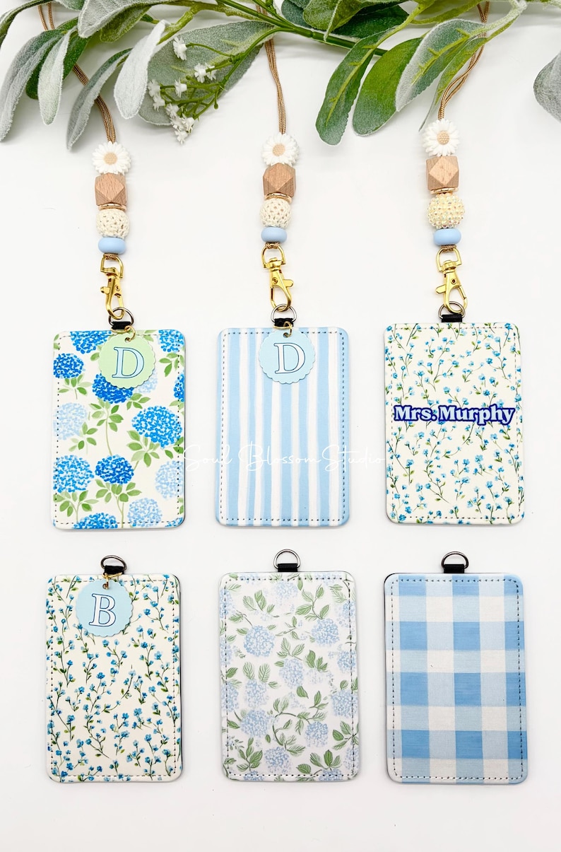 May include: Six rectangular ID badge holders with lanyards featuring beaded accents. The holders display various blue and white patterns including hydrangeas, stripes, floral prints, and gingham. Some holders feature circular letter tags or the text Mrs. Murphy.