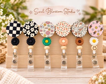 May include: Six circular badge reels with diverse patterns including black and white checkers, floral prints, and smiley faces. Each features a small flower bead, a wooden spacer, and a clear plastic strap with a metal snap button closure.
