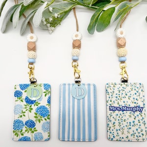 May include: Three rectangular ID badge holders with lanyards featuring beaded accents. The holders display blue hydrangea patterns, light blue stripes, and a floral print with the text Mrs. Murphy. Each lanyard includes a gold clasp and beads.