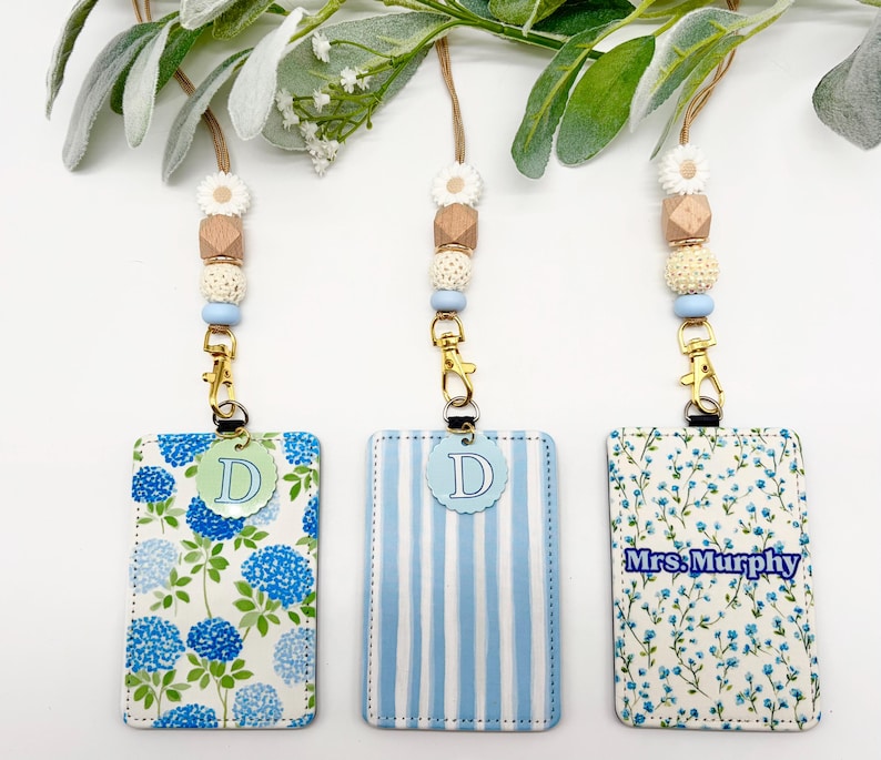 May include: Three rectangular ID badge holders with lanyards featuring beaded accents. The holders display blue hydrangea patterns, light blue stripes, and a floral print with the text Mrs. Murphy. Each lanyard includes a gold clasp and beads.