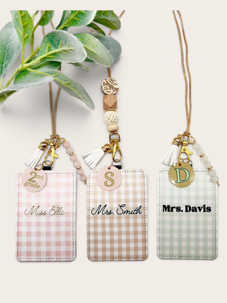 May include: Three rectangular ID badge holders with gingham patterns in pink, tan, and light green. Each holder features a gold-toned lanyard, a white tassel, a beaded accent, and a circular charm with the text 2nd grade, S, or D, and names.