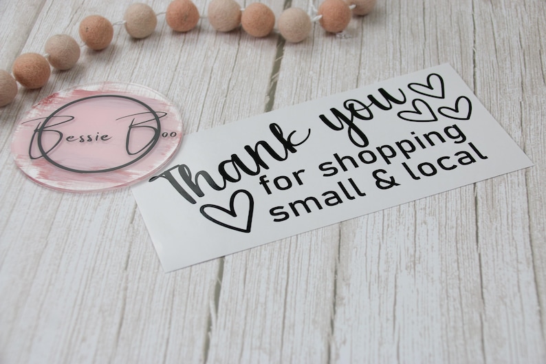 May include: A rectangular white card with black text that reads Thank you for shopping small & local with three heart icons, alongside a circular pink acrylic disc featuring the black text Bessie Boo inside a circular border.