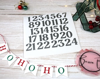 May include: A white sheet of paper with black numbers 1 through 24 printed on it. The numbers are arranged in rows of four. A red and green Christmas banner with the word "HO HO HO" printed on it is in the foreground.