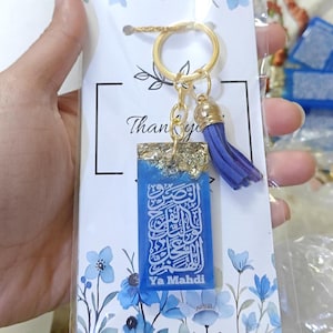 May include: A blue resin keychain with gold leaf accents and a tassel. The keychain features Arabic calligraphy and the text "Ya Mahdi".