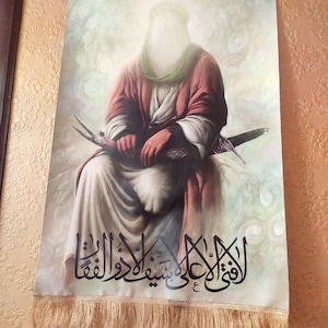 May include: A religious image depicting a figure in a white robe and a green turban, holding a sword. The background is a light blue with white clouds. The image is framed with a gold border and has a fringe at the bottom. The text in the image reads "الْقَوِيُّ عَلَىٰ شَيْئٍ وَهُوَ عَلَىٰ كُلِّ شَيْءٍ قَدِيرٌ".