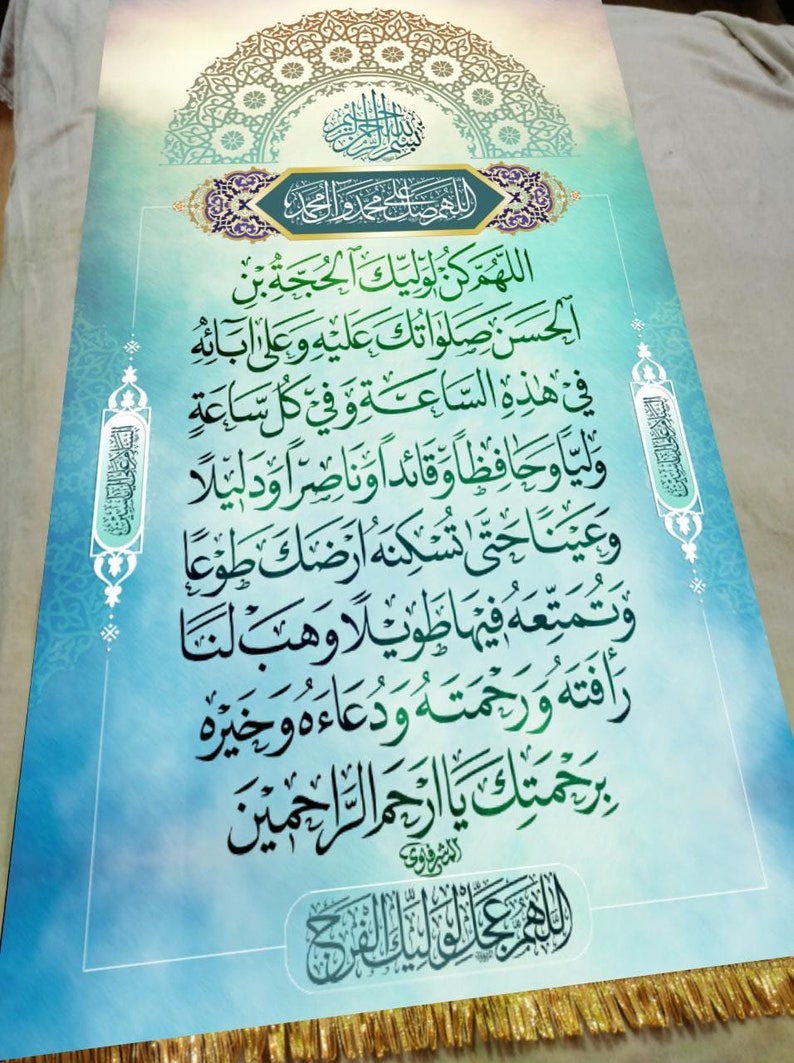 May include: A blue and green Islamic prayer banner with Arabic calligraphy. The text reads "Allahumma kun li waliyyik al-hujjah ibn al-hasan salatuk alaihi wa ala abaihi fi hadhihi al-sa'ah wa fi kulli sa'ah waliyyan wa hafizhan wa qa'idan wa nasiran wa dalilan wa 'ainan hatta tuskinahu ardhak tau'an wa tumatti'ahu fiha tawilan wa hab lana rafatahu wa rahmatahu wa du'a'ahu wa khai rahu bi rahmatak ya arhamar rahimin al-mushrifawi allahumma 'ajjil li waliyyik al-furj".