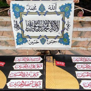 May include: Two black framed prints with gold and red calligraphy in Arabic script. The prints feature a gold dome and a red flag. The top print has the text "Allah Muhammad" and "Hassan Hussein".