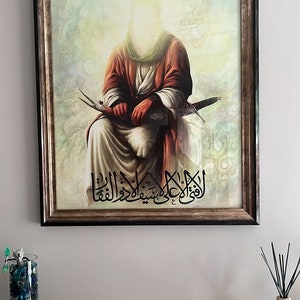May include: A framed painting depicting a religious figure wearing a red robe, seated with a sword in their lap. The painting is set against a cloudy background with Arabic text at the bottom.
