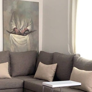 May include: A brown sectional sofa with three beige throw pillows. A white side table with a silver metal frame sits in front of the sofa. A painting of a person in a white robe hangs on the wall behind the sofa.