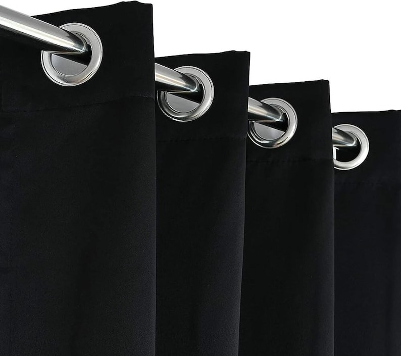 Puede incluir: Primer plano de cortinas negras con ojales plateados y una barra de cortina plateada. La tela es de color negro liso, y los ojales est&aacute;n espaciados uniformemente a lo largo del borde superior. Las cortinas cuelgan en pliegues verticales.