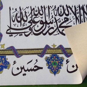 May include: A white canvas print with black Arabic calligraphy and colorful floral designs. The print features the phrase "La ilaha illa Allah Muhammadur Rasulullah" in a decorative frame.