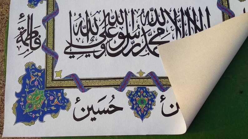 May include: A white canvas print with black Arabic calligraphy and colorful floral designs. The print features the phrase "La ilaha illa Allah Muhammadur Rasulullah" in a decorative frame.