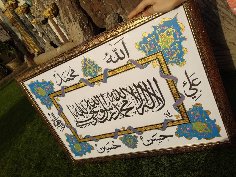May include: A framed piece of Islamic calligraphy art with intricate floral designs in blue, green, and gold. The calligraphy is in Arabic and reads "Allah" and "Muhammad".