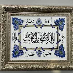 May include: A framed artwork with a white background and intricate blue and gold floral designs. The artwork features Arabic calligraphy in black ink, including the words "Allah" and "Muhammad".