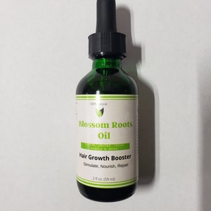 Könnte beinhalten: Eine grüne Glasflasche mit schwarzem Tropfer. Die Flasche ist mit "Blossom Roots Oil" beschriftet und trägt den Hinweis "Hair Growth Booster" mit den Inhaltsstoffen "Castor, Jojoba, Argan, Marula & Herbs". Die Flasche trägt außerdem die Aufschrift "Stimulate, Nourish, Repair" und "2 fl oz. (59 ml)".