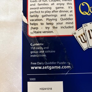 May include: A close-up of a blue game box with the word "Quiddler" in yellow. The box includes text about the game and its contents, including 118 cards and instructions. Several game cards are visible.