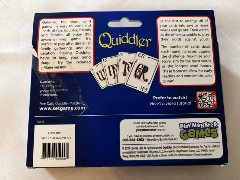 May include: A Quiddler card game box with a blue background. The box features the game's logo and images of cards spelling "WINNER". Text on the box describes the game's rules and contents, including 118 cards and instructions.