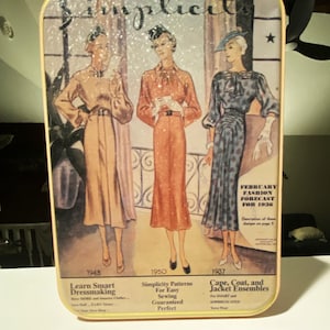 May include: Vintage metal tin featuring a fashion illustration from 1936. The design showcases three women in dresses, with text including "Simplicity" and "February Fashion Forecast." The tin has a yellow border and a slightly distressed appearance, evoking a retro aesthetic.