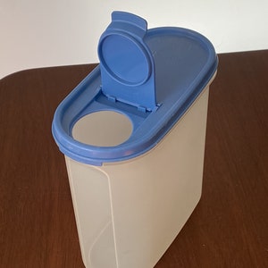 May include: A clear plastic container with a blue lid and a hinged opening. The container is oval shaped and has a smooth surface.