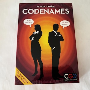 May include: A sealed board game box titled "Codenames" with the author's name, Vlada Chvatil, at the top. The box features silhouettes of a man and woman, with speech bubbles saying "Top Secret" and "Word Game". The box is a best-selling party game.