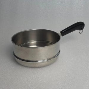 May include: A stainless steel saucepan with a polished finish and a single black handle. The handle features a small metal loop at the end for hanging. The pan has a cylindrical body with a slightly rounded base and a smooth, reflective surface.