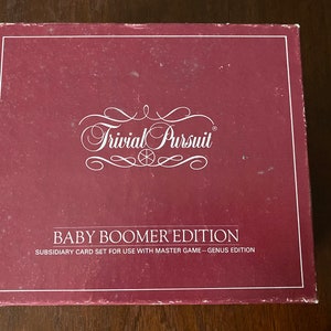 May include: A maroon box for the Trivial Pursuit Baby Boomer Edition game. The box has white text and a white border. The text includes the game title and edition information.
