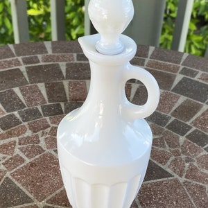 May include: White milk glass bottle with a fluted design and a round stopper. The bottle has a handle and is perfect for serving oil or vinegar.
