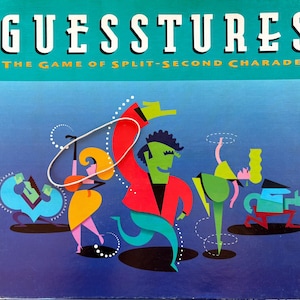 May include: A board game box with the title "GUESSTURES" in white capital letters above the subtitle "THE GAME OF SPLIT-SECOND CHARADES." The box features colorful cartoon figures in various poses, set against a blue and purple gradient background.