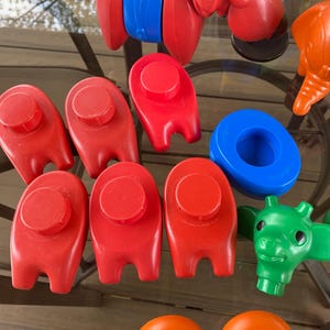 May include: A set of colorful plastic toys, including a red elephant, a blue and red stacking toy, and several red and blue pieces with knobs. The toys are on a wooden surface.