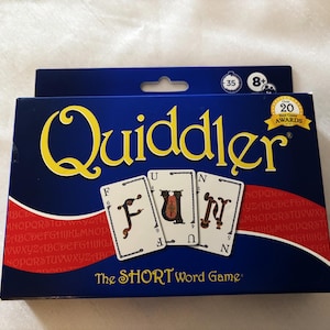 May include: A blue game box with the word "Quiddler" in yellow script. The box features three cards spelling "FUN". The text "The SHORT Word Game" is below the cards. The box also has a "20 Game Awards" seal.