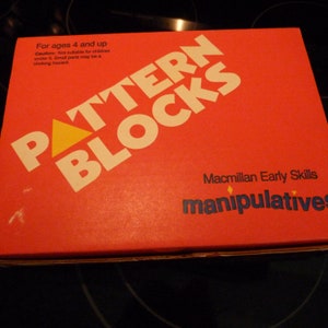 May include: Red box with the words "PATTERN BLOCKS" in white letters. The box also has the words "Macmillan Early Skills manipulatives" in blue letters. The box is for ages 4 and up and has a warning about choking hazards for children under 3.