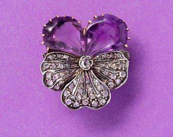 May include: A silver and gold brooch in the shape of a flower with two large amethyst stones and smaller diamond accents.
