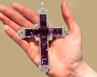 May include: A large cross pendant featuring deep purple square-cut amethyst gemstones set in a silver-toned metal frame. The cross is embellished with numerous small, clear, sparkling stones along the edges and at the top bail attachment.
