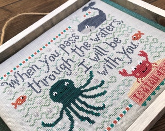 May include: A framed cross-stitch embroidery with a white background and green, blue, and red accents. The embroidery features a whale, an octopus, and a crab with the text "When you pass through the waters I will be with you".