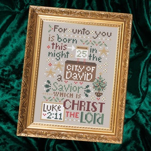 Puede incluir: Un diseño de punto de cruz enmarcado con un fondo beige y bordado en marrón, verde y rojo. El diseño presenta un mensaje navideño que dice "Porque hoy os ha nacido en la ciudad de David un Salvador, que es Cristo el Señor" e incluye el versículo bíblico "Lucas 2:11".