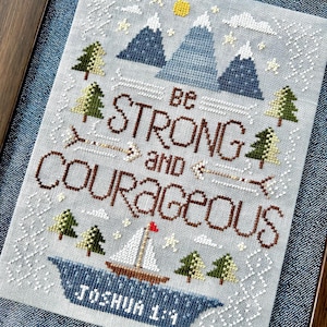 Puede incluir: Obra de arte de punto de cruz en un marco de madera. El diseño presenta montañas, árboles, un velero y el texto "Be Strong and Courageous" con la referencia "Joshua 1:9". La paleta de colores incluye tonos de azul, marrón, verde y blanco.