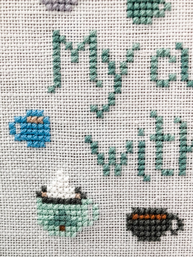May include: Cross-stitch embroidery on white fabric with the words "my tea with" in green thread and images of teacups in blue, green, and gray thread.