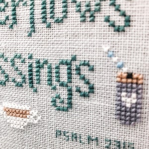 May include: Cross-stitch embroidery with teal blue thread, depicting a cup of coffee and the words "Fellows Greetings" with the text "PSALM 23:6" below.