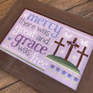 May include: Cross stitch embroidery with a purple background and the text "mercy there was great and grace was free". The design includes three crosses, white doves, and purple flowers.