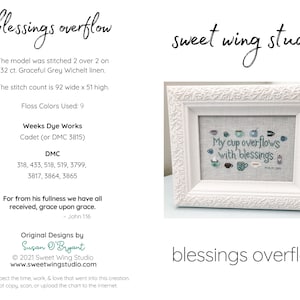 May include: A white frame with a cross-stitch design inside. The design features a cup overflowing with blessings. The text "My cup overflows with blessings" is stitched in blue thread. The text "John 1:16" is stitched in smaller blue thread. The frame is on a white background. The text "blessings overflow" is written in black below the frame.