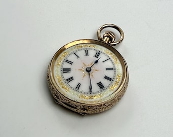 May include: A gold pocket watch with a white face, black Roman numerals, and delicate gold detailing. The watch has a small loop at the top and is likely an antique or vintage item.