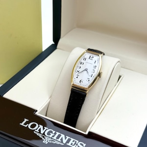 May include: A gold-toned Longines watch with a rectangular face and black leather band. The watch face is white with black numerals and hands. The watch is presented in a black and cream-colored box with the Longines logo.