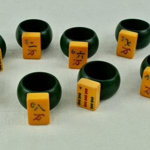 May include: Eight green and yellow napkin rings with Chinese characters and numbers on the yellow tiles. The rings are made of wood.